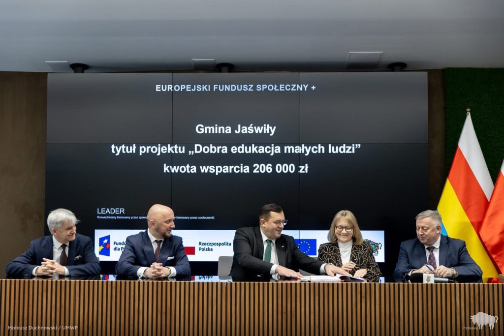 Zdjęcie przedstawia pięć osób siedzących za stołem i podpisujących umowę o dofinansowanie projektu. 